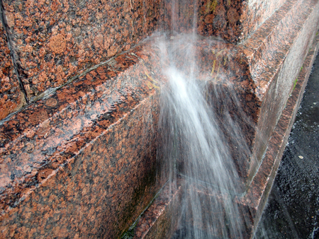 A strong jet of water flowing from the downspout on the granite wall during the rainstormの写真素材