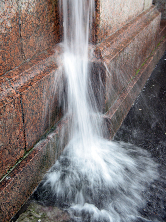 A strong jet of water flowing from the downspout on the granite wall during the rainstormの写真素材