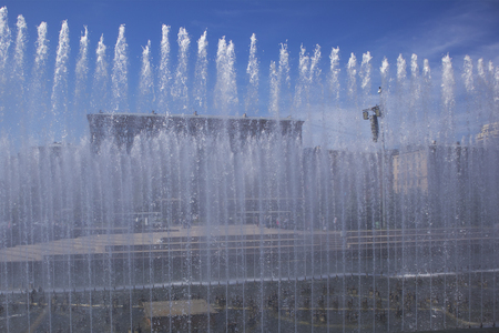 Summer cityscape with street and square in the distance trough the wall of water from the fountainsの写真素材