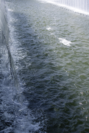 Wide glassy water flow falling down into the spacious fountain reservoirの写真素材