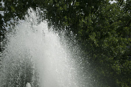 Large top of the fountain jet gushing upwards against green foliageの写真素材