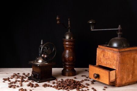 Wooden vintage manual coffee mills and pepper mill with coffee beans scattered on a wooden surfaceの写真素材