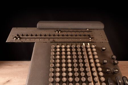 Old counting mechanism, dusty vintage arithmometer standing on a wooden board against black fabricの写真素材