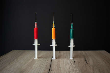 Three medical syringes with colored liquid standing upright on a wooden boardの写真素材