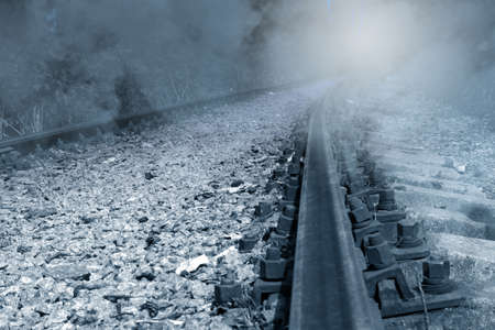 Old rusty abandoned railway in fog going off into the distance for a turn with mystical light, monochrome imageの写真素材