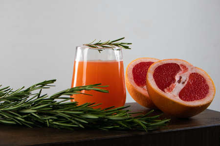 Two halves of red orange, rosemary sprig and glass of orange juice lying on a wooden table against light backgroundの写真素材