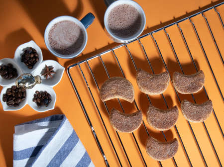 Two mugs of cacao, semilunar candied cookies on a metal grate, striped towel and spices. Top view...
