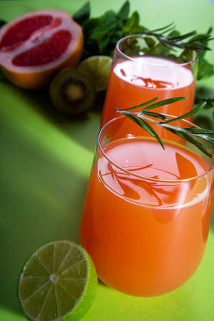 Composition of glasses with orange juice, cut red orange, lime, kiwi, rosemary and mint leaves on a...
