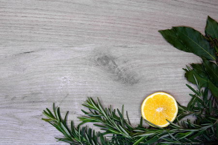 Light wooden board framed with fresh rosemary sprigs, bay leaves and lemon half, design templateの写真素材