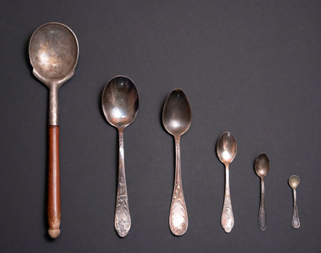 The set of vintage spoons of different metals and sizes against gray backgroundの写真素材