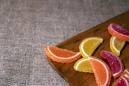Pile of colorful candied marmalade in the shape of citrus slices lying on the sackcloth and wooden boardの写真素材