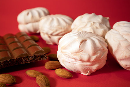 Few white delicate zephyrs with porous chocolate bar and scattering peeled almond against bright red saturated backgroundの写真素材