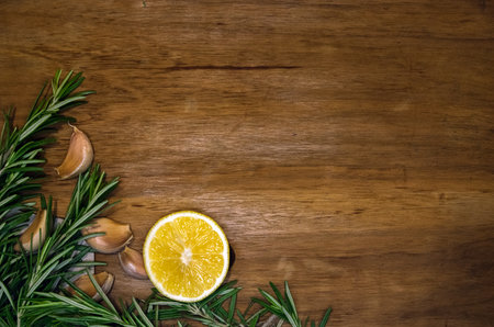 Fresh rosemary sprigs, garlic cloves and lemon half on a dark wooden board, postcard or invitation templateの写真素材