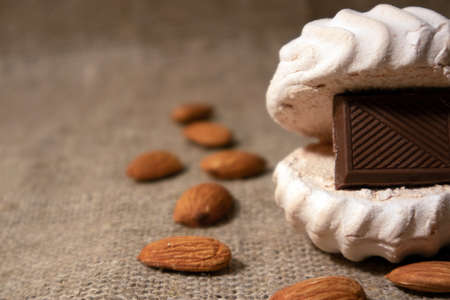 White zephyr with tile of dark chocolate inside and scattered peeled almonds lying on a sack clothの写真素材