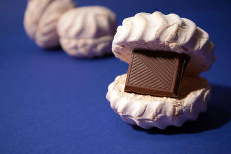 White zephyr with tile of dark chocolate inside against trendy blue backgroundの写真素材