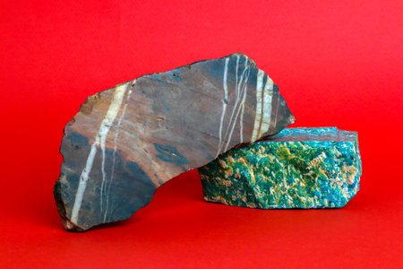 Two pieces of natural raw minerals, amazonite and jasper, against bright red backgroundの写真素材