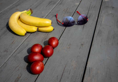 Mix composition with painted easter eggs, bunch of ripe bananas and sunglasses lying on an old wooden surfaceの写真素材