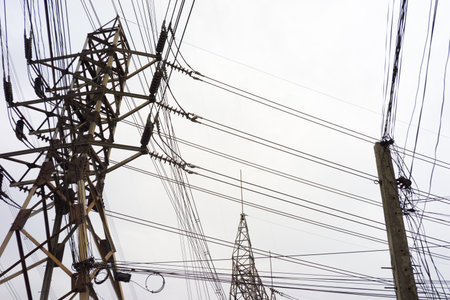 Highâvoltage electric transmission towers and utility poles with numerous power lines crisscrossing against a cloudy sky.の写真素材