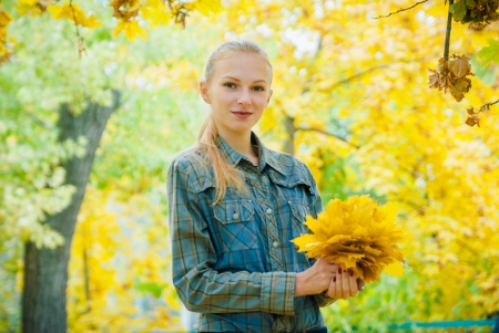 Young woman with autumn leaves in hands and fall yellow maple garden backgroundの写真素材