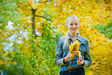 Young woman with autumn leaves in hands and fall yellow maple garden backgroundの写真素材