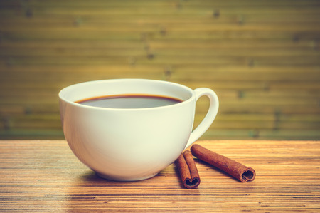 Composition with white cup of coffee and cinnamon on green bamboo background. Retro toning.の写真素材