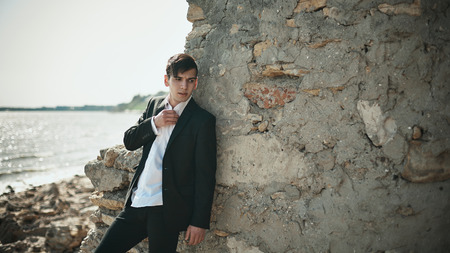 Fashion photo of a man on a seaside standing near the wall in the black suit
