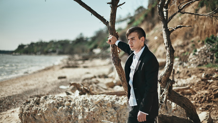 Fashion photo of a man on a seaside standing near the tree in the black suitの写真素材