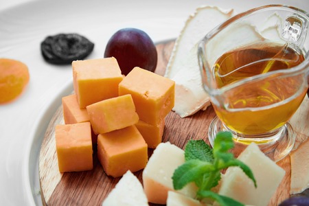 Cheese, grapes, mint, pitcher of oil, prunes and dried apricots are laid out on a wooden boardの写真素材