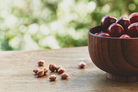 Photo of cherry berries in the wooden bowl on the wooden table and fruit pits near it on the green bokeh backgroundの写真素材