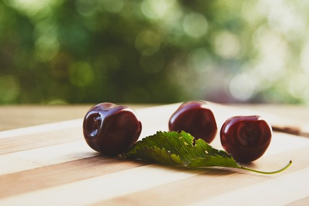 Photo of cherry berries and green leaf on the wooden cutting board on the grren bokeh backgroundの写真素材