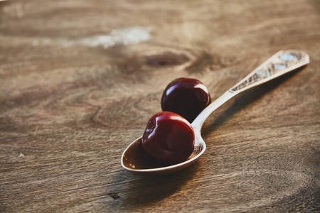 Close-up photo of two red cherry berries, lying near the spoon