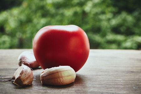 Photo of red tomato on the green stem and three garlic cloves on the blured backgroundの写真素材