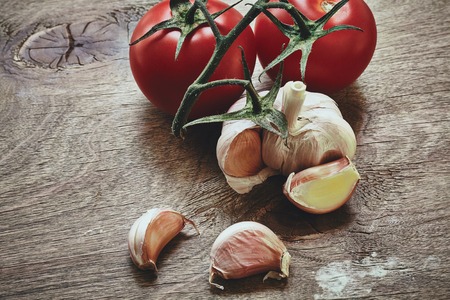 from above photo of red tomatoes on the green stem and three garlic cloves on the wooden tableの写真素材