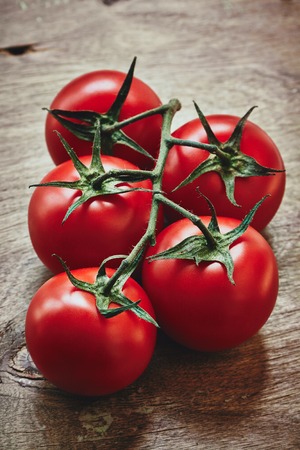from above vertical photo of red tomatoes on the green stem on the wooden tableの写真素材