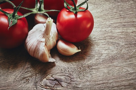 From above photo of red tomatoes on the green stem and three garlic cloves on the wooden tableの写真素材