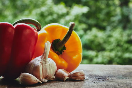 Horizontal photo of red and orange peppers, garlic bulb and cloves on the green blured backgroundの写真素材