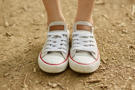 Close-up photo of girl's legs in white shoes on ground background