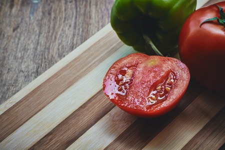 From above photo of green pepper and red fresh tomatoe with the green stem and half of it on the cutting boardの写真素材