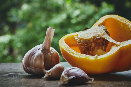 Composition with half of orange pepper, garlic bulb and cloves on the green blured backgroundの写真素材