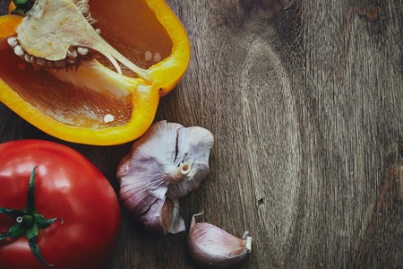 From above photo of half of orange pepper, red fresh tomatoe with the green stem, garlic bulb and clove on the wooden tableの写真素材