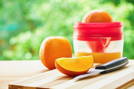 Knife, juicer and oranges on the wooden cutting board on green blurred background