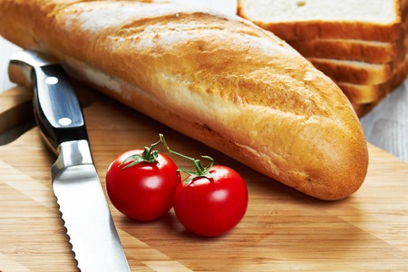 Baguette, two tomatoes, toasts and knife on wooden cutting boardの写真素材