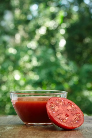 Composition of half of tomato and juice in the glass bowl on the wooden tableの写真素材