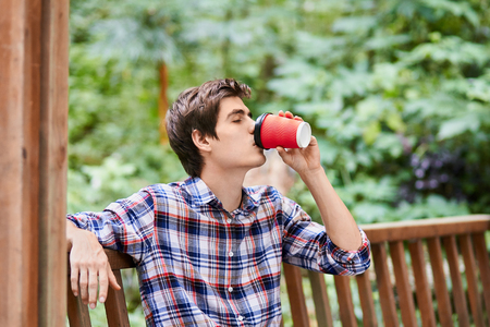 Man in the forest in wooden summerhouse with red paper cupの写真素材