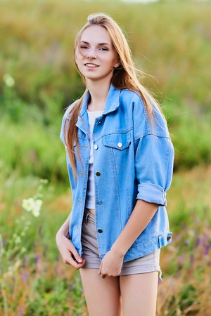 Happy young girl wearing blue jeans jacket in the fieldの写真素材