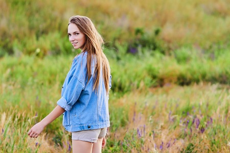 Happy young girl wearing blue jeans jacket in the fieldの写真素材