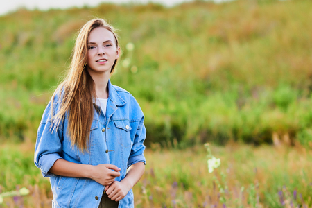 Happy young girl wearing blue jeans jacket in the fieldの写真素材