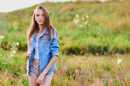 Happy young girl wearing blue jeans jacket in the fieldの写真素材
