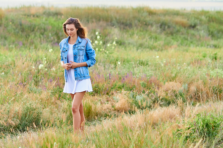 Happy young girl wearing blue jeans jacket and dress in the fieldの写真素材
