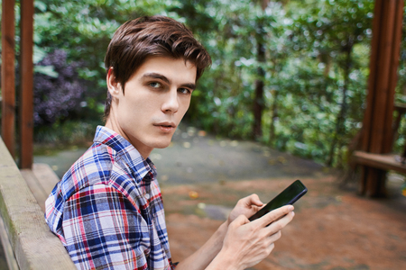 Man is sitting in the wooden pavilion and looking at the cellphone in the forestの写真素材